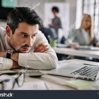 stock-photo-young-businessman-leaning-on-his-desk-and-feeling-bored-while-surfing-the-net-on-a-computer-at-work-1337445686
